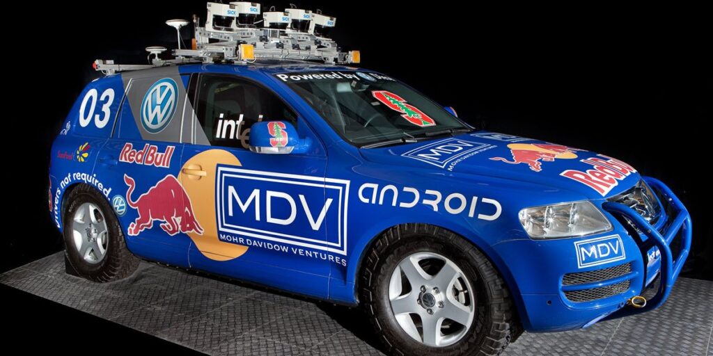 photo-of-a-blue-car-covered-in-company-logos-with-an-array-of-sensors-mounted-to-the-roof.jpg